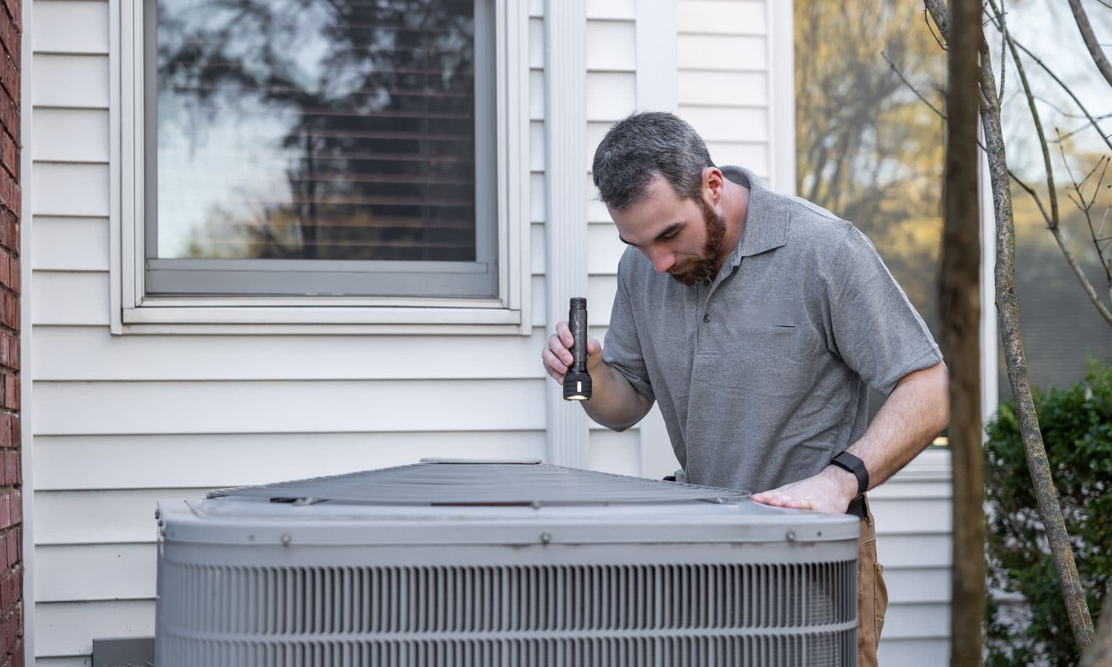 Technician inspecting an outdoor air conditioning unit beside a home