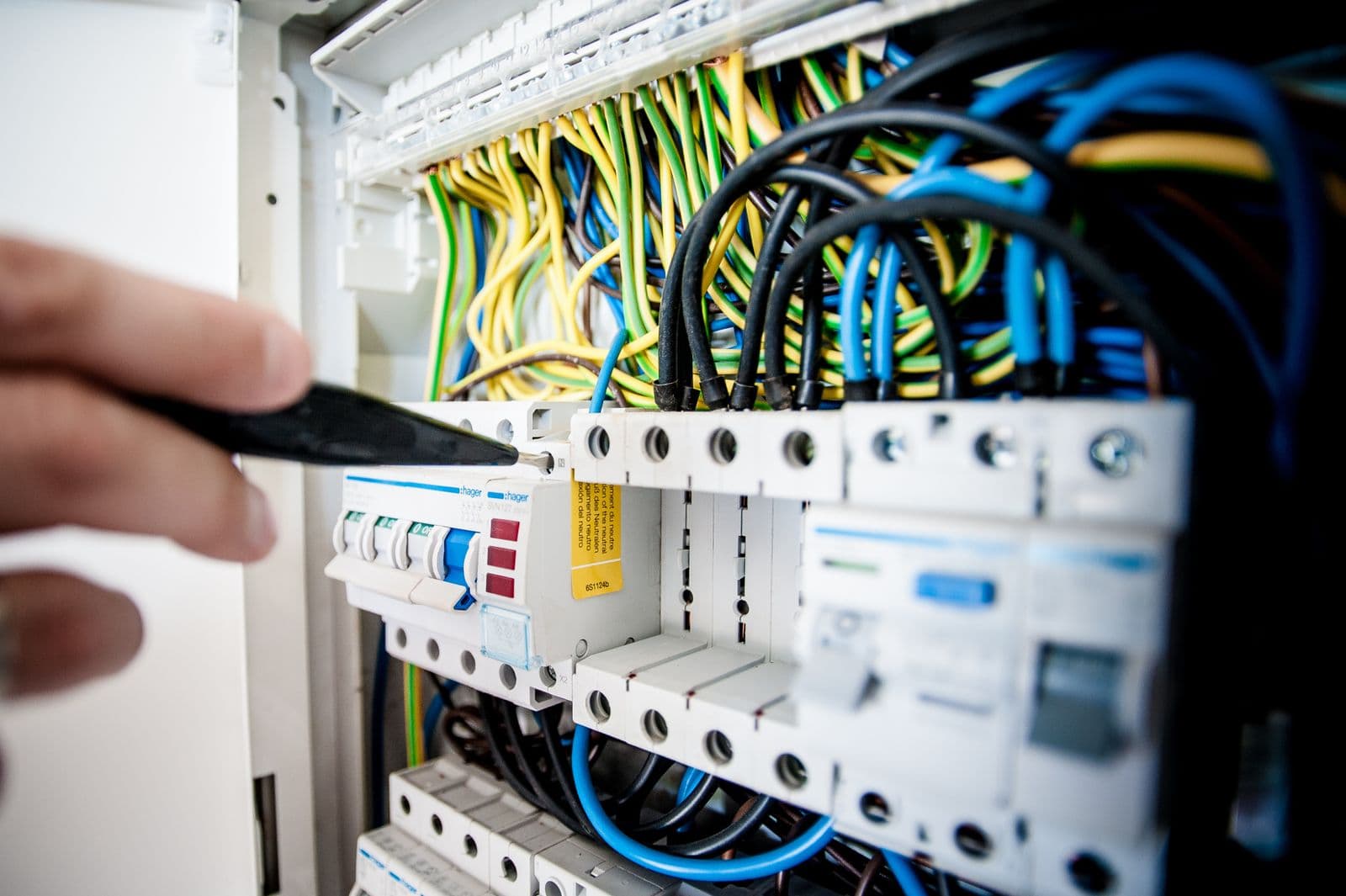 Electrician working inside an open breaker panel filled with color-coded wiring