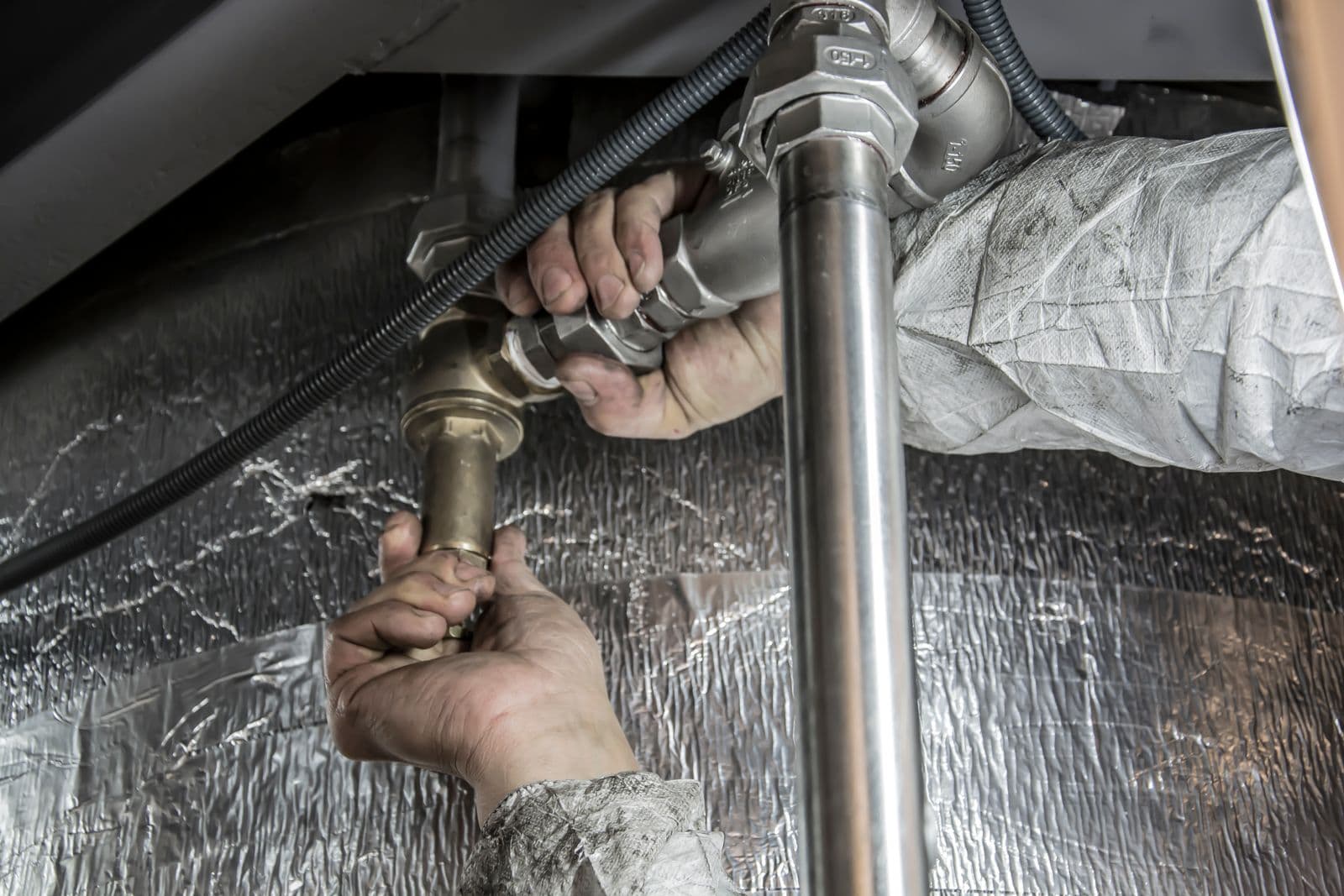 Plumber's hands tightening steel supply pipes beneath a sink